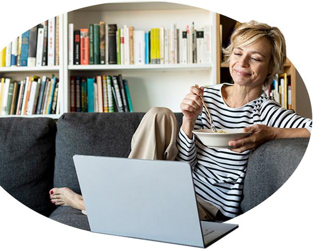 Woman eating while looking at her laptop on the couch